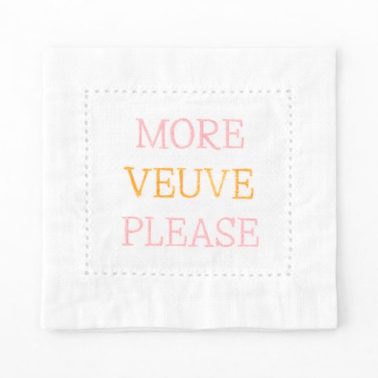 Embroidered white linen cocktail napkin featuring “More Veuve Please” phrase, styled with champagne glasses for bridal showers, girls’ brunches, and elegant entertaining.