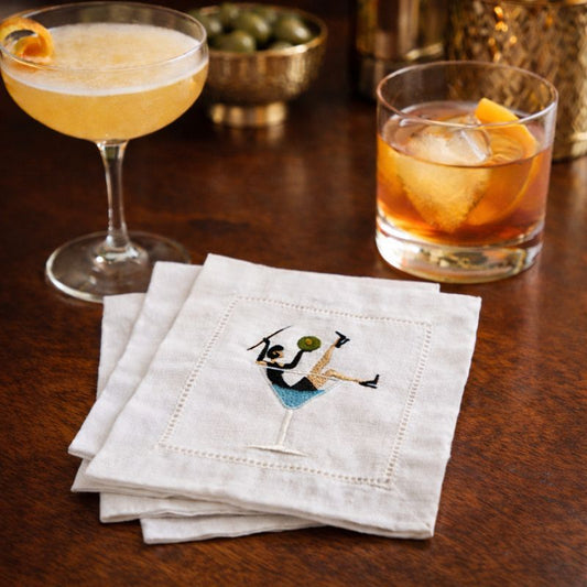 Embroidered cocktail napkin with martini glass design featuring a playful figure holding an olive.